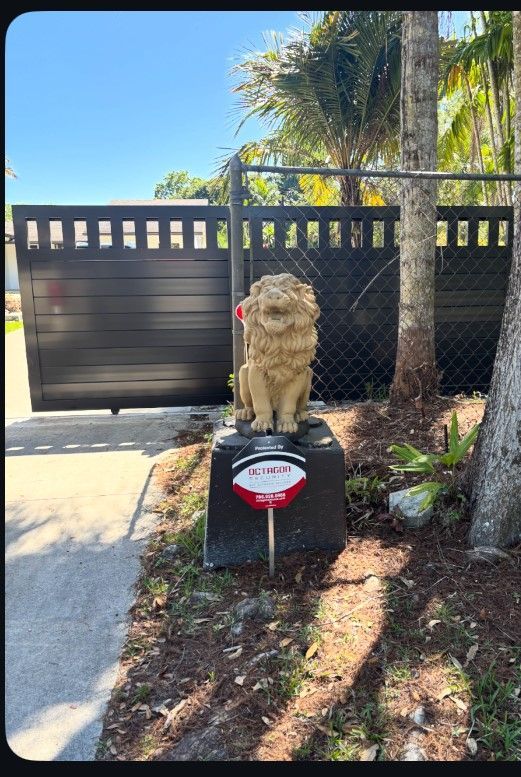 Lion statue on black base, in front of a black gate, and a security system sign.