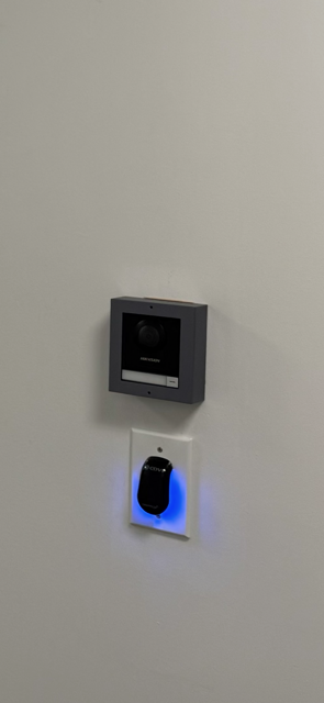 A gray control panel and light switch with blue glowing light are mounted on a white wall.