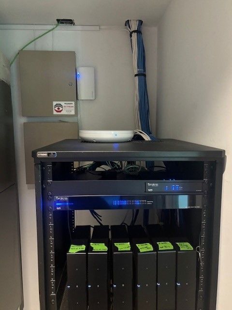 Network rack with servers, networking gear, and cable management in a white closet.