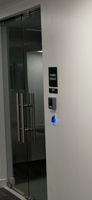 Glass door with handle, access control panel, and illuminated blue button.