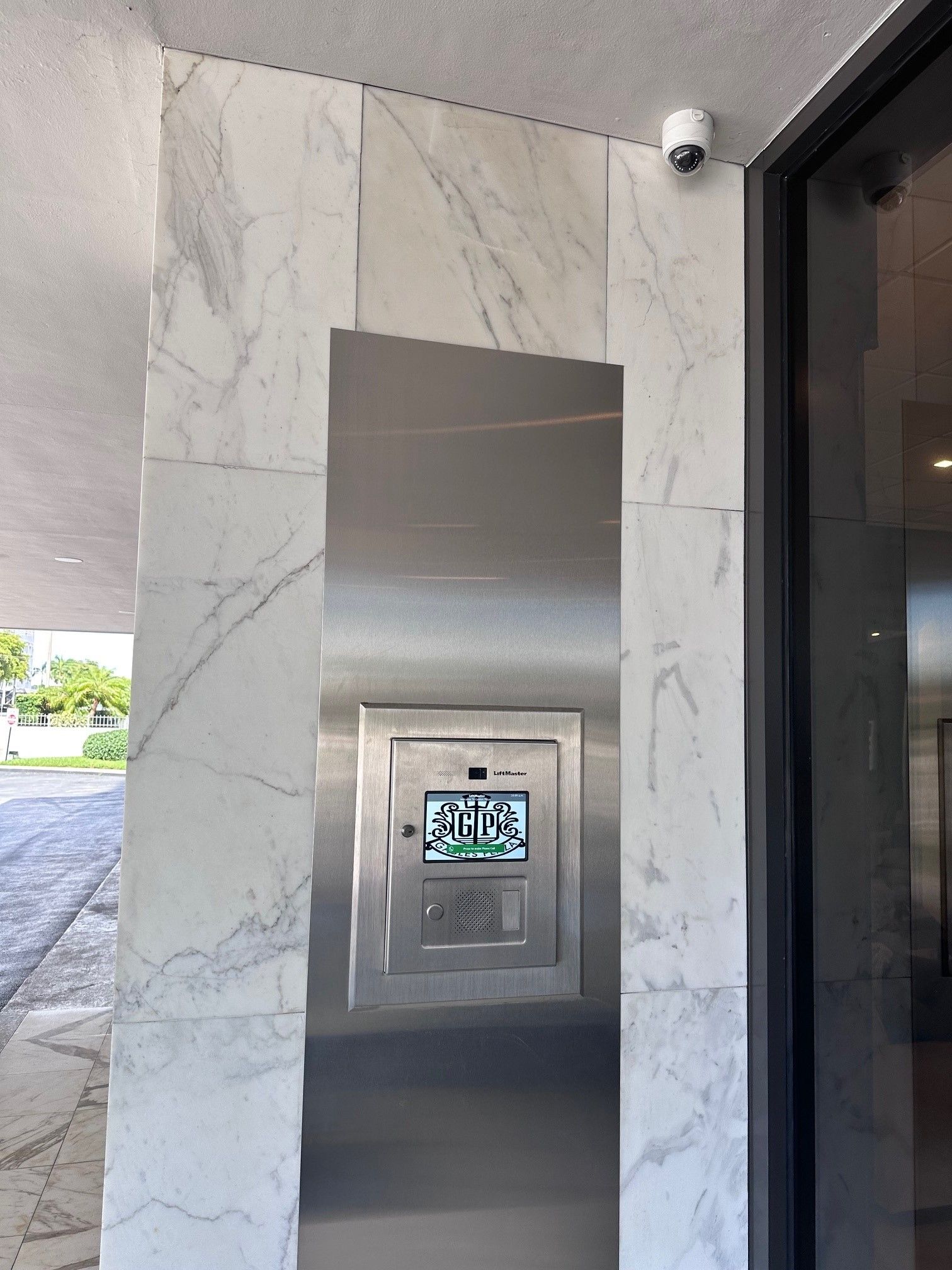 Stainless steel building entry panel with screen and camera on marble pillar.