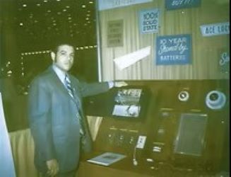 Man in suit pointing to a display of electronic devices at a trade show.