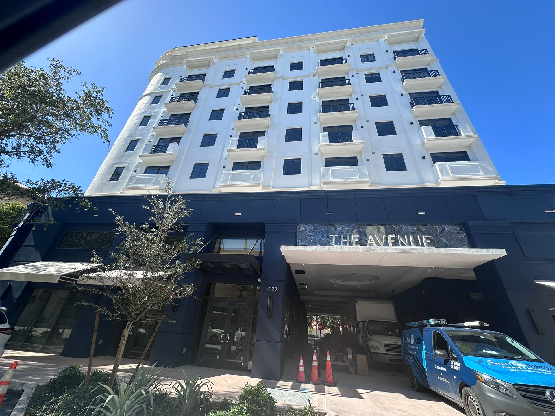The Avenue hotel building with white facade and dark blue base. Sunny day, a van parked below.