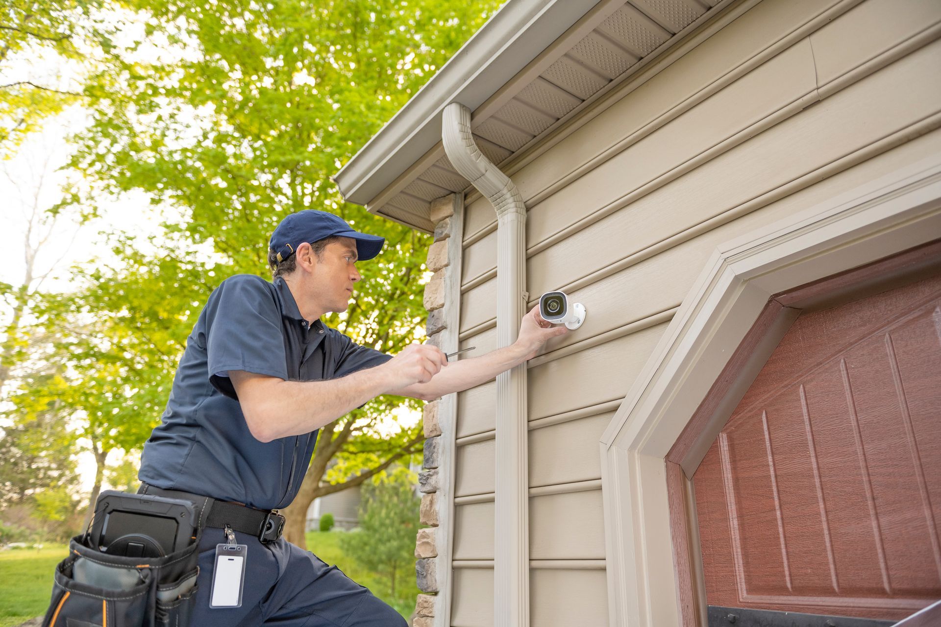 Man in uniform installing security camera on the side of a house.