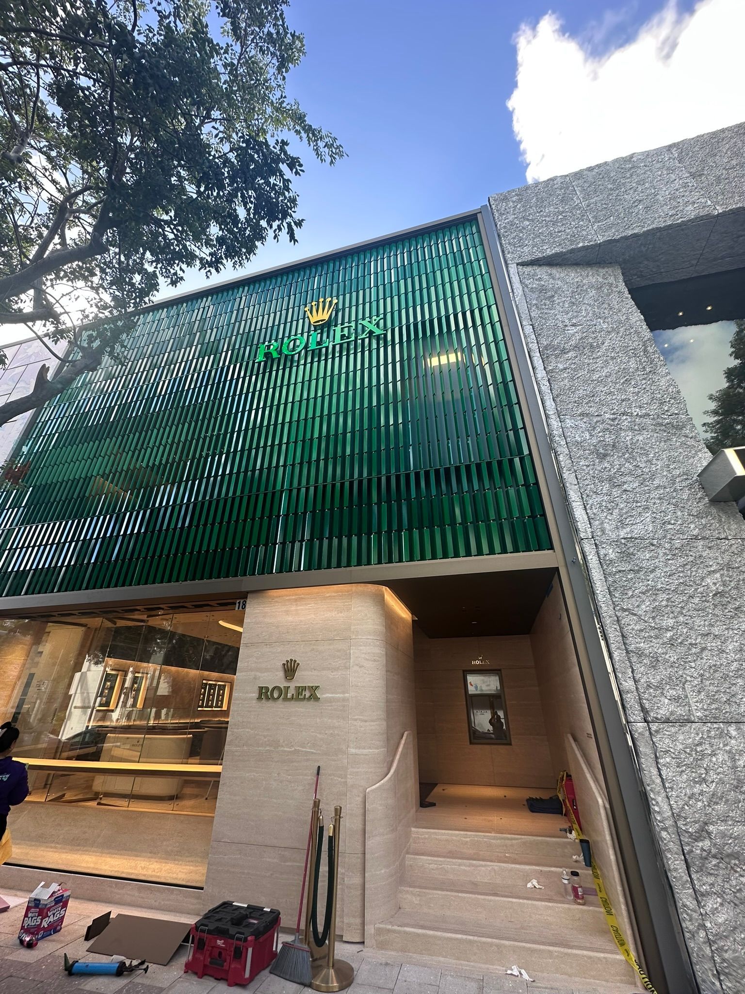 Rolex store exterior with green facade, stone accents, and stairs leading to the entrance.