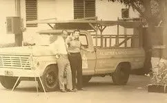 Two people stand next to a yellow pickup truck with tools and the words 