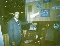 Man in suit points to display panel at a trade show booth, likely for electronics.