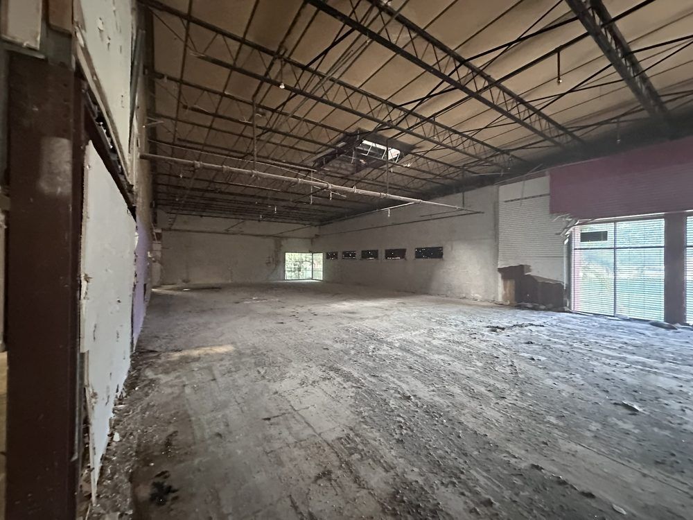 Interior view of a dilapidated, empty warehouse space with exposed beams and debris on the floor.