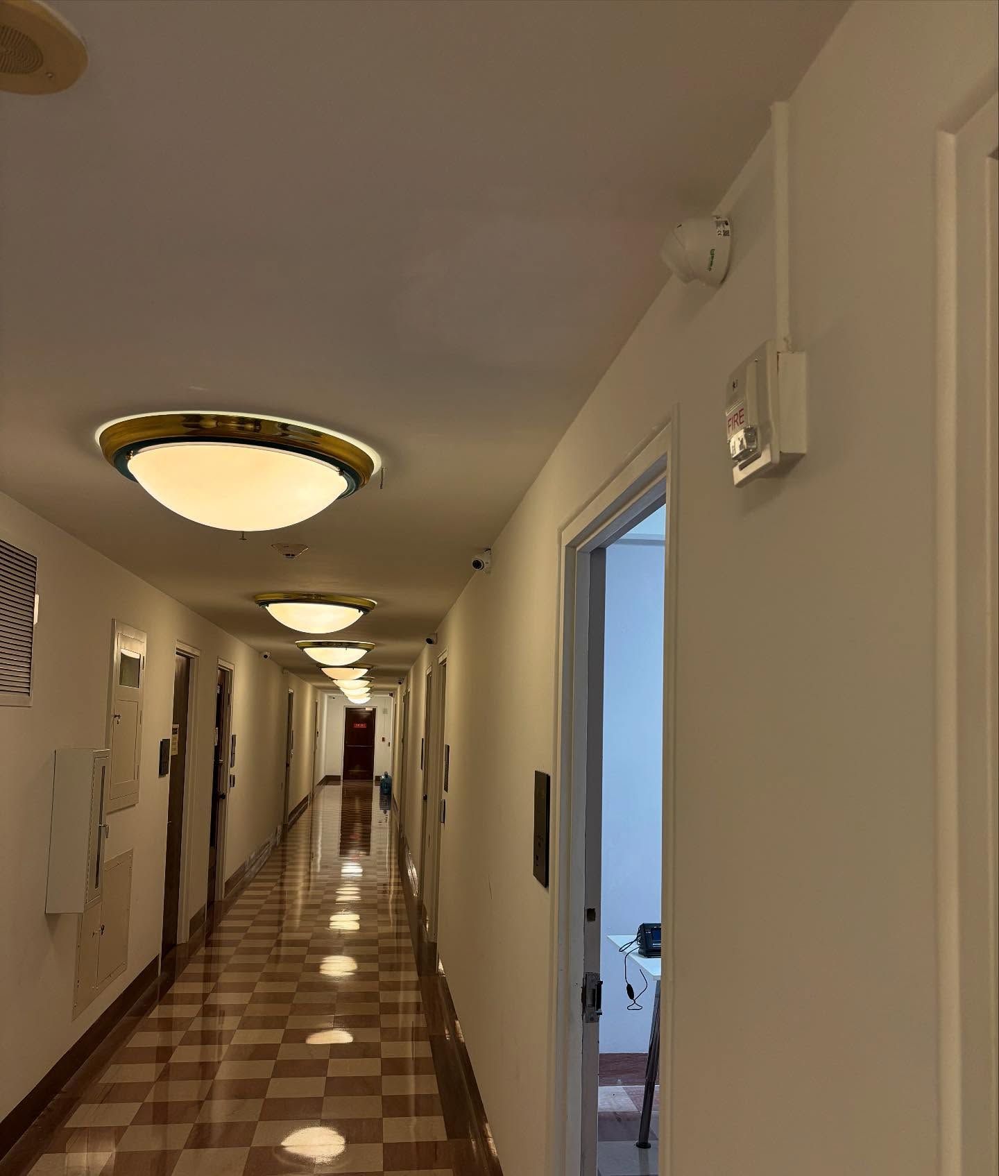 Long hallway with closed doors, overhead lights, and a patterned floor.