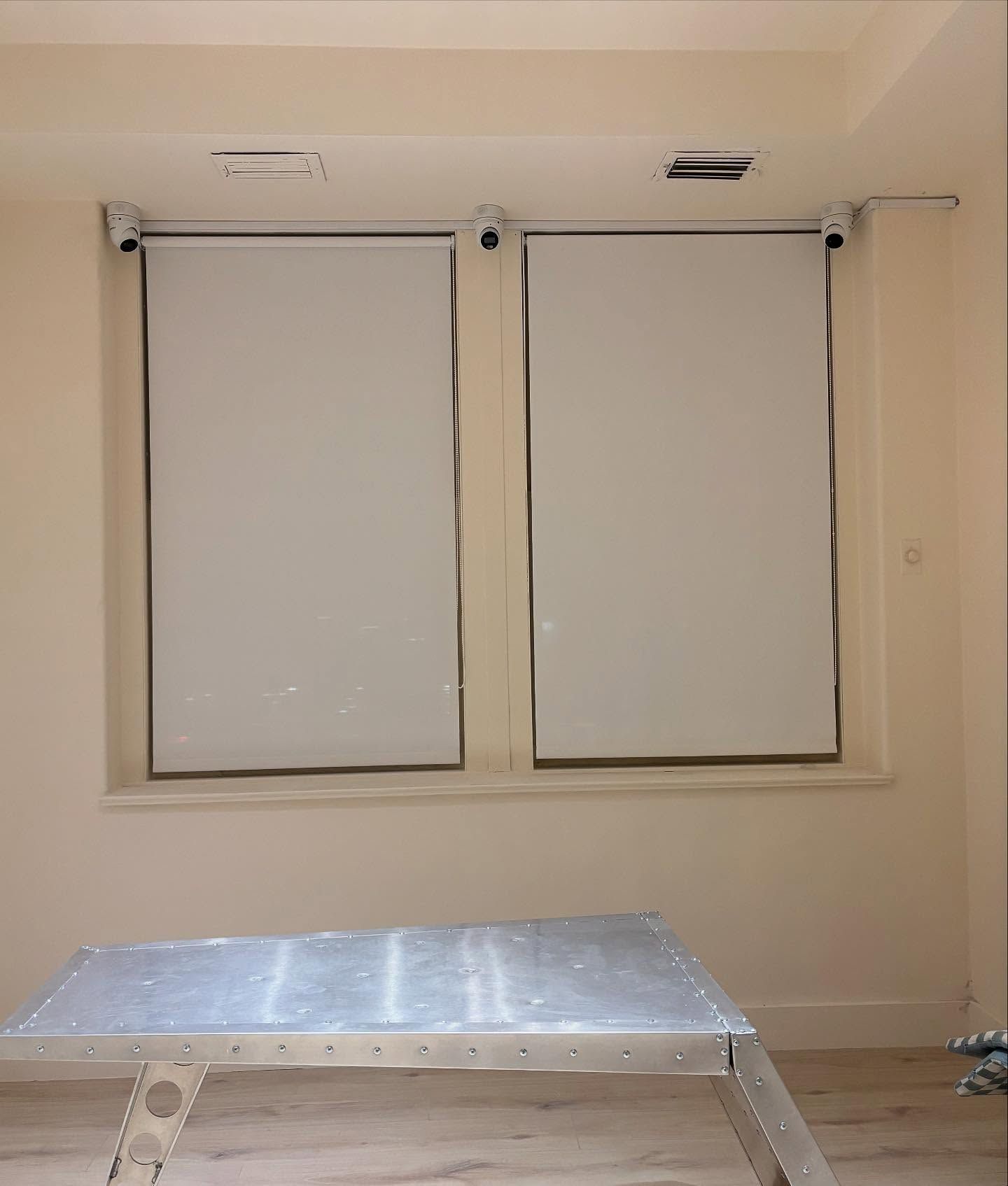 Two closed, light-colored window shades in a room with a stepladder in front of them.