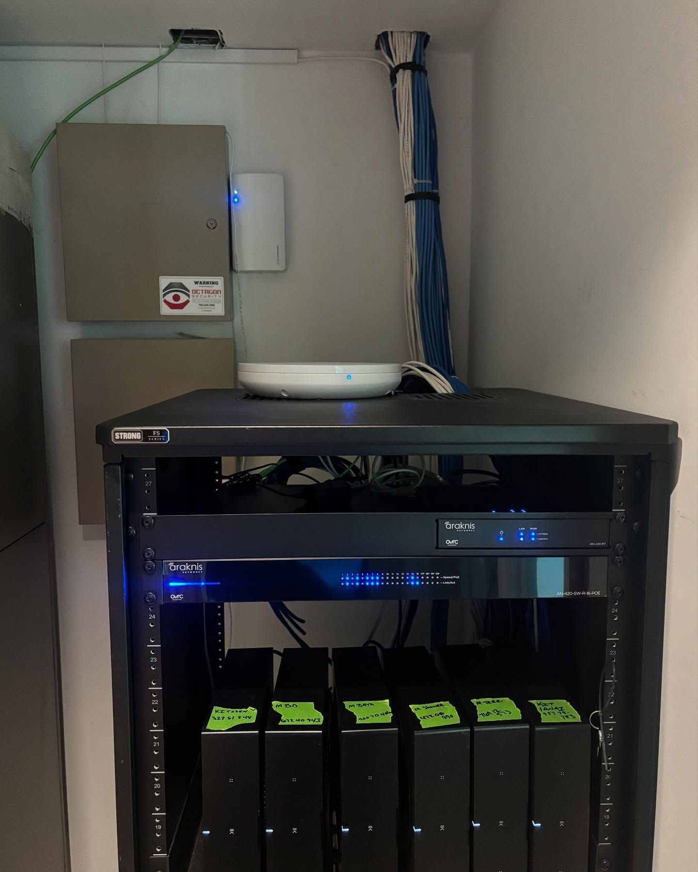 Network equipment rack with a wireless access point, surrounded by wall-mounted panels and cables.