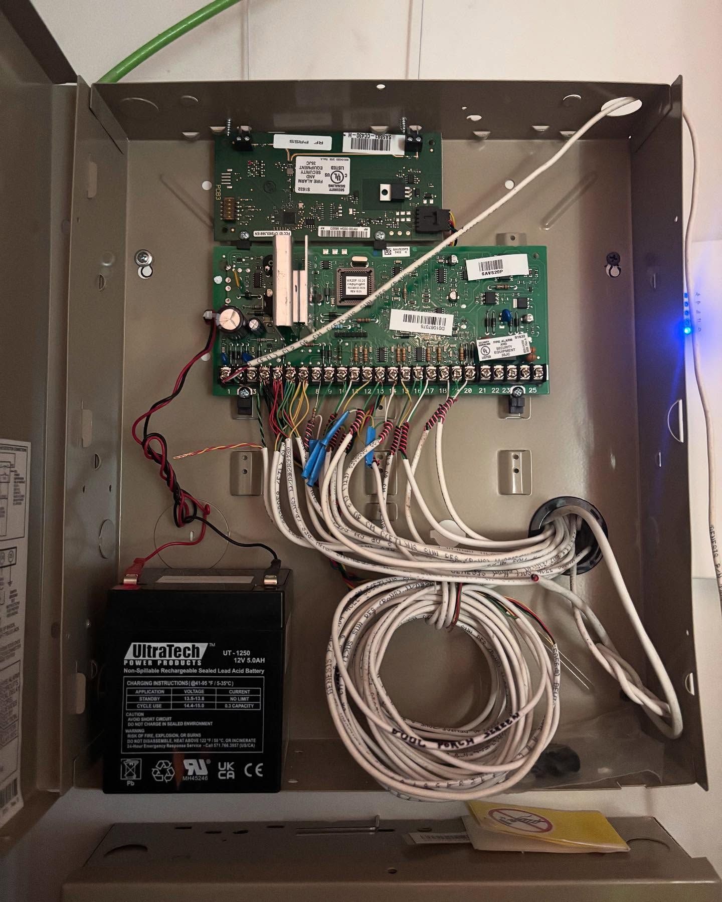 Security system control panel with circuit boards, battery, and wires.