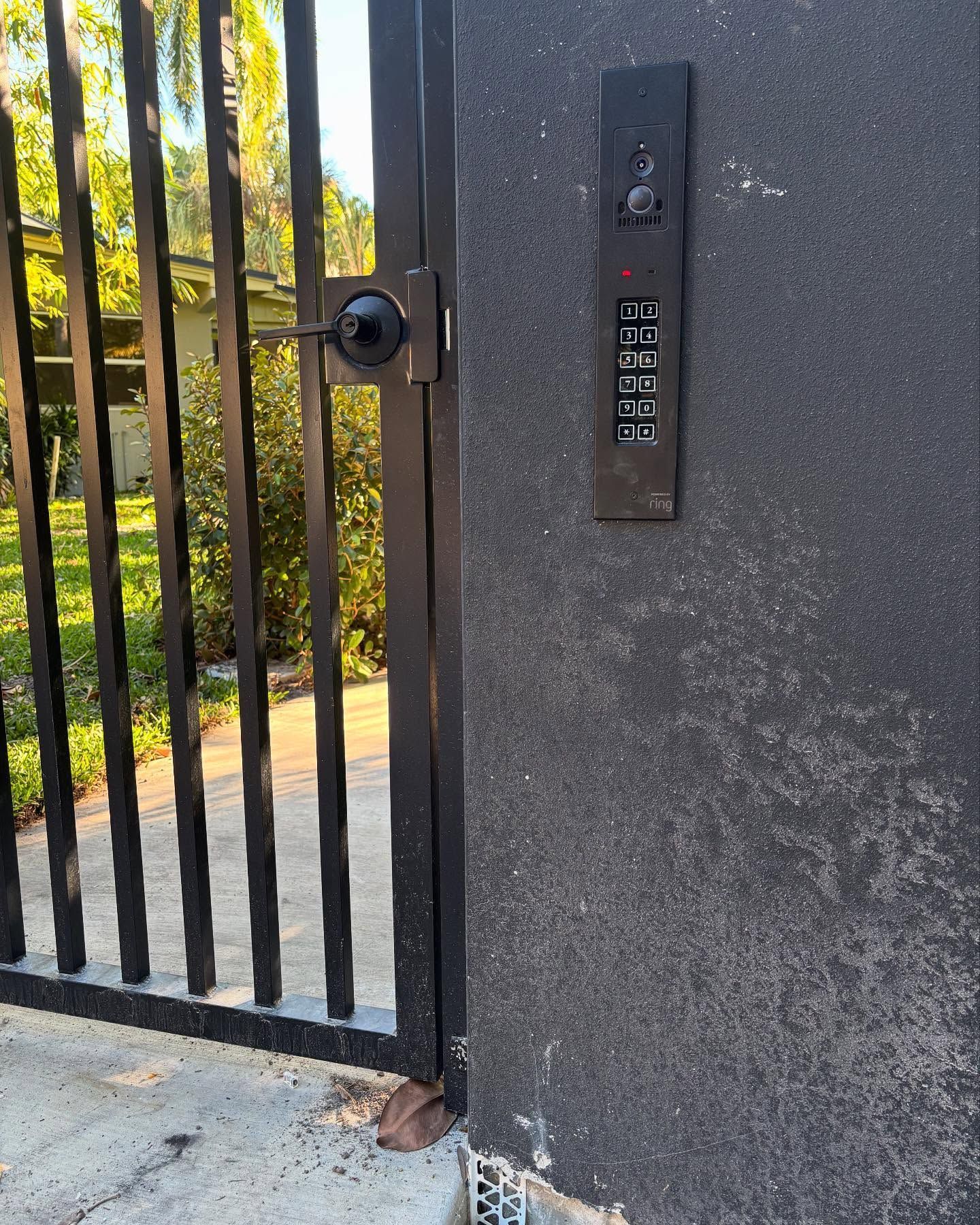 Black gate with keypad, camera, mounted on a dark textured wall.
