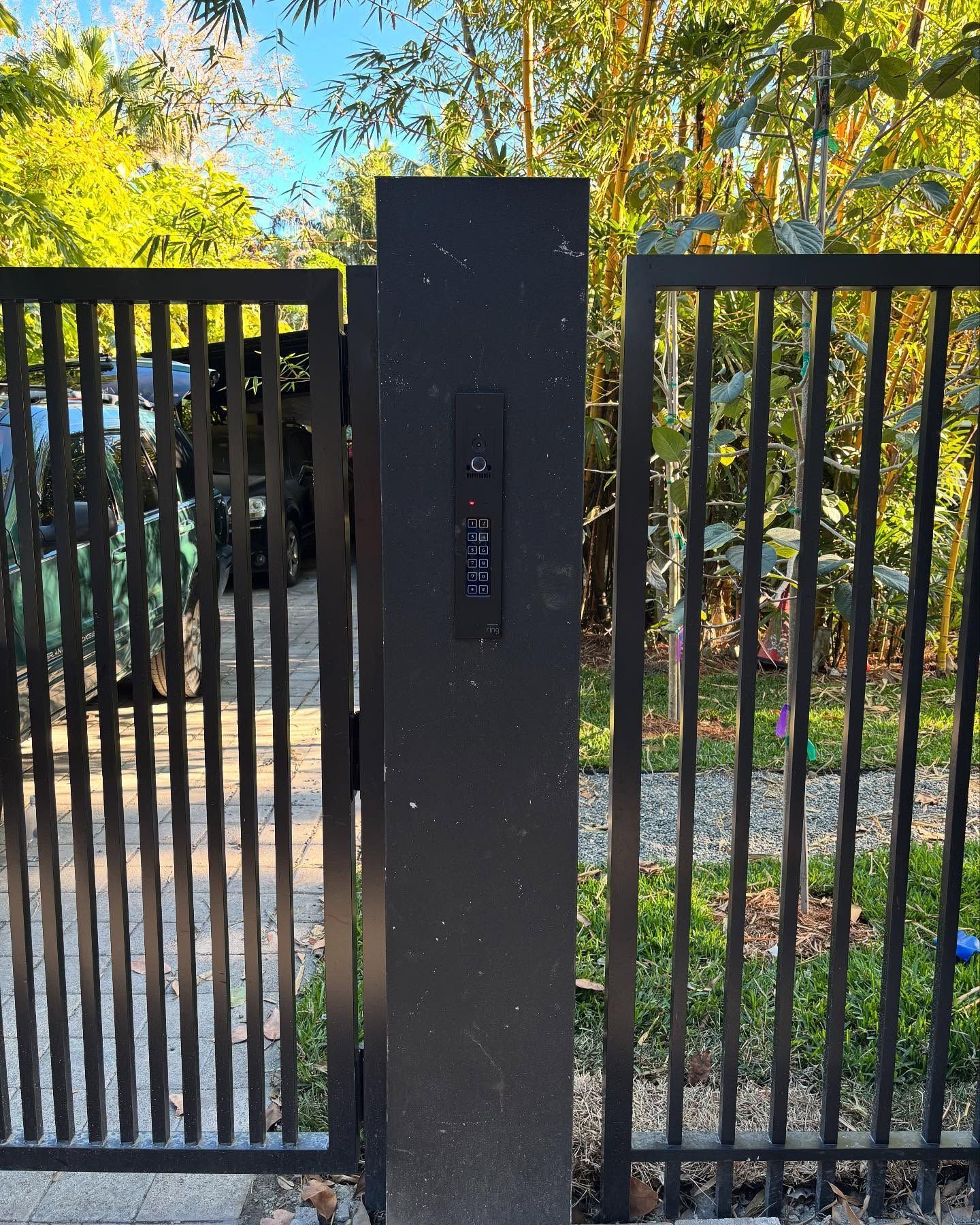 Black metal gate with vertical bars and a tall black post with a keypad.