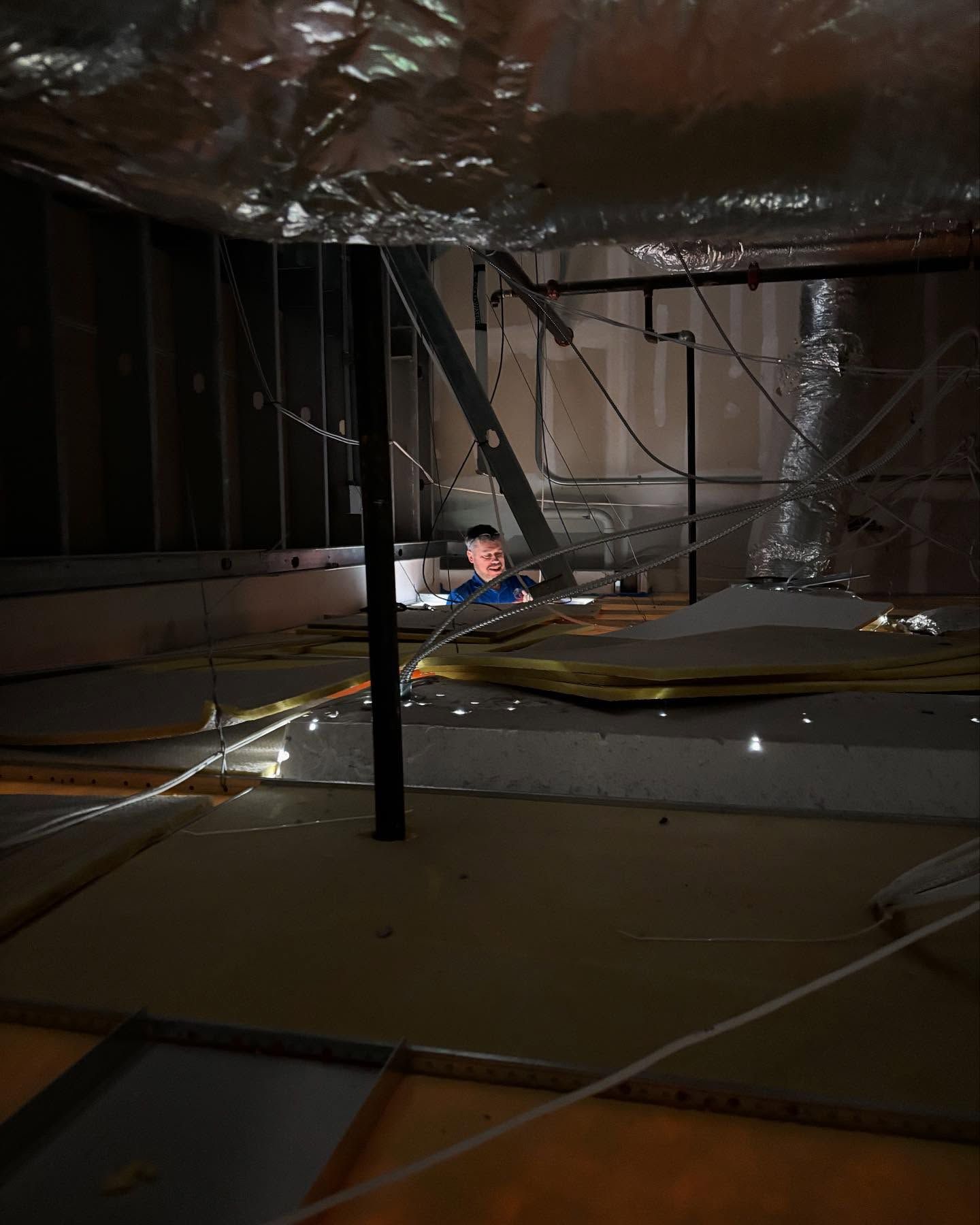 Child peering from a dark crawl space filled with wires, insulation, and ductwork.