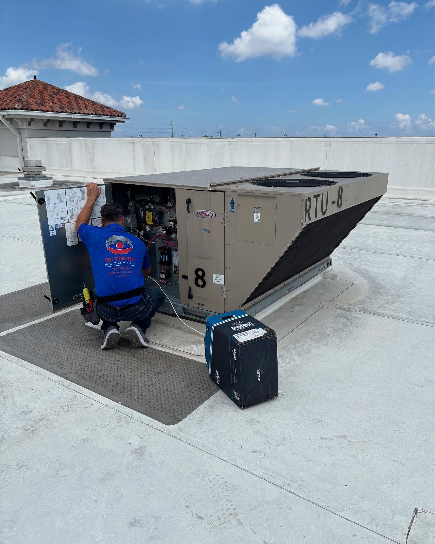 HVAC technician kneels near rooftop unit on a white roof, examining it. The unit is tan and black. Blue sky.
