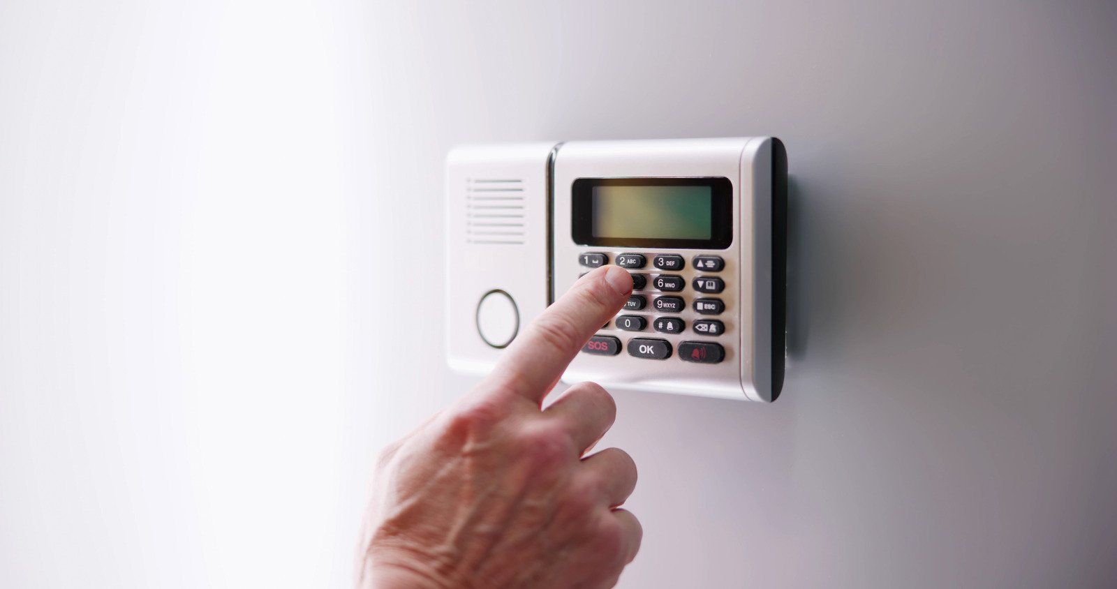 Hand entering code on a white security system keypad mounted on a wall.