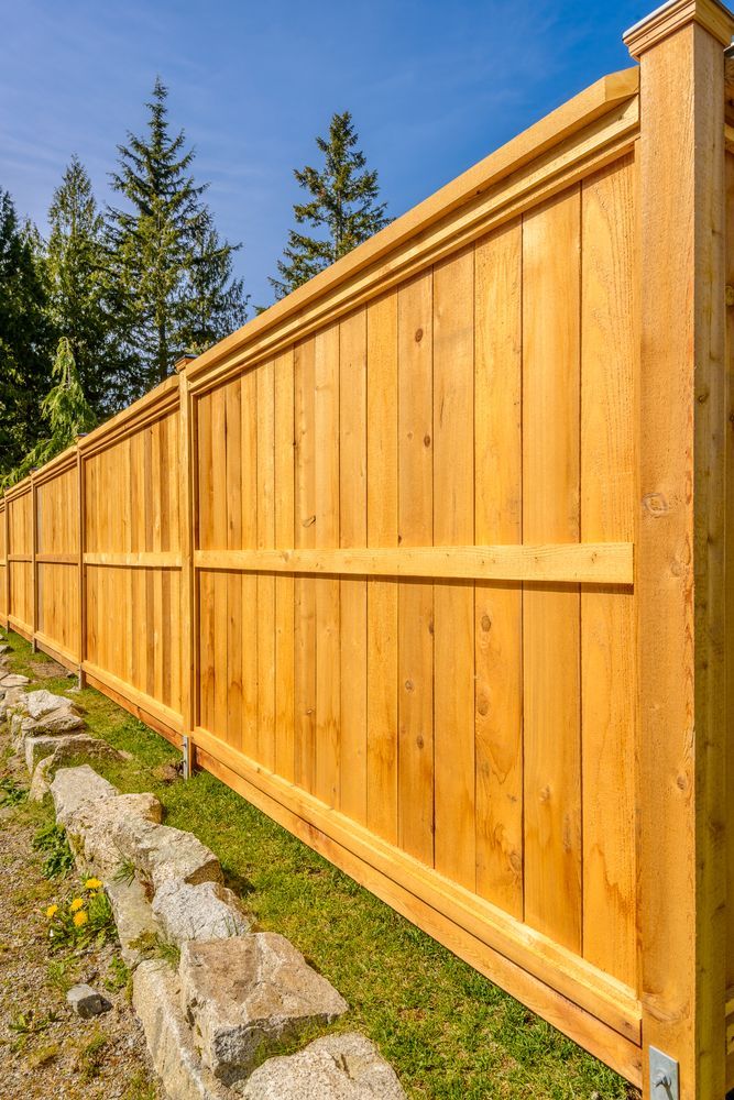 A wooden fence is surrounded by grass and rocks on a sunny day.