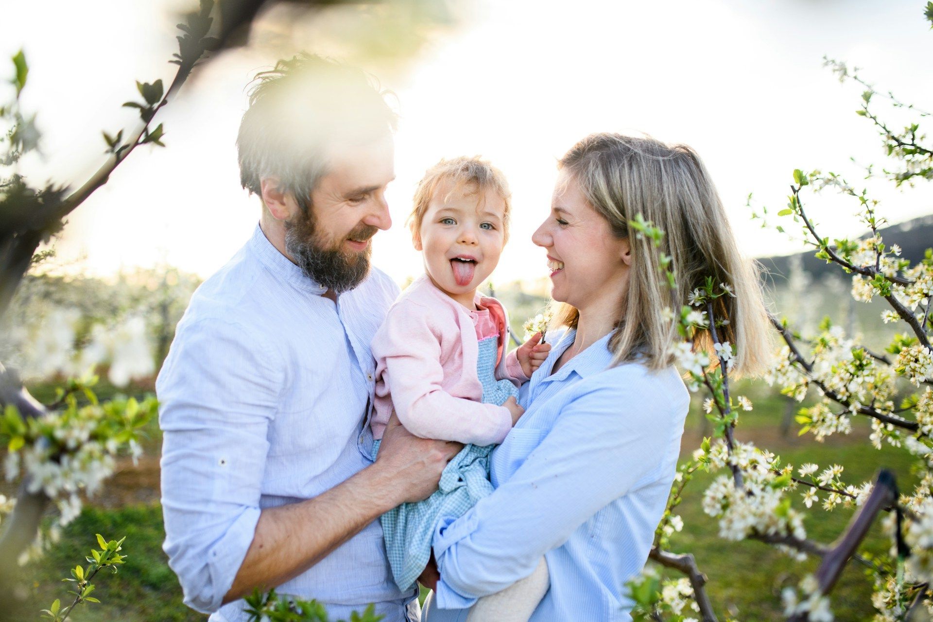 Family of three smiles amongst flowering tree branches; child sticks out tongue.