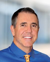 A man in a blue shirt and yellow tie is smiling for the camera.