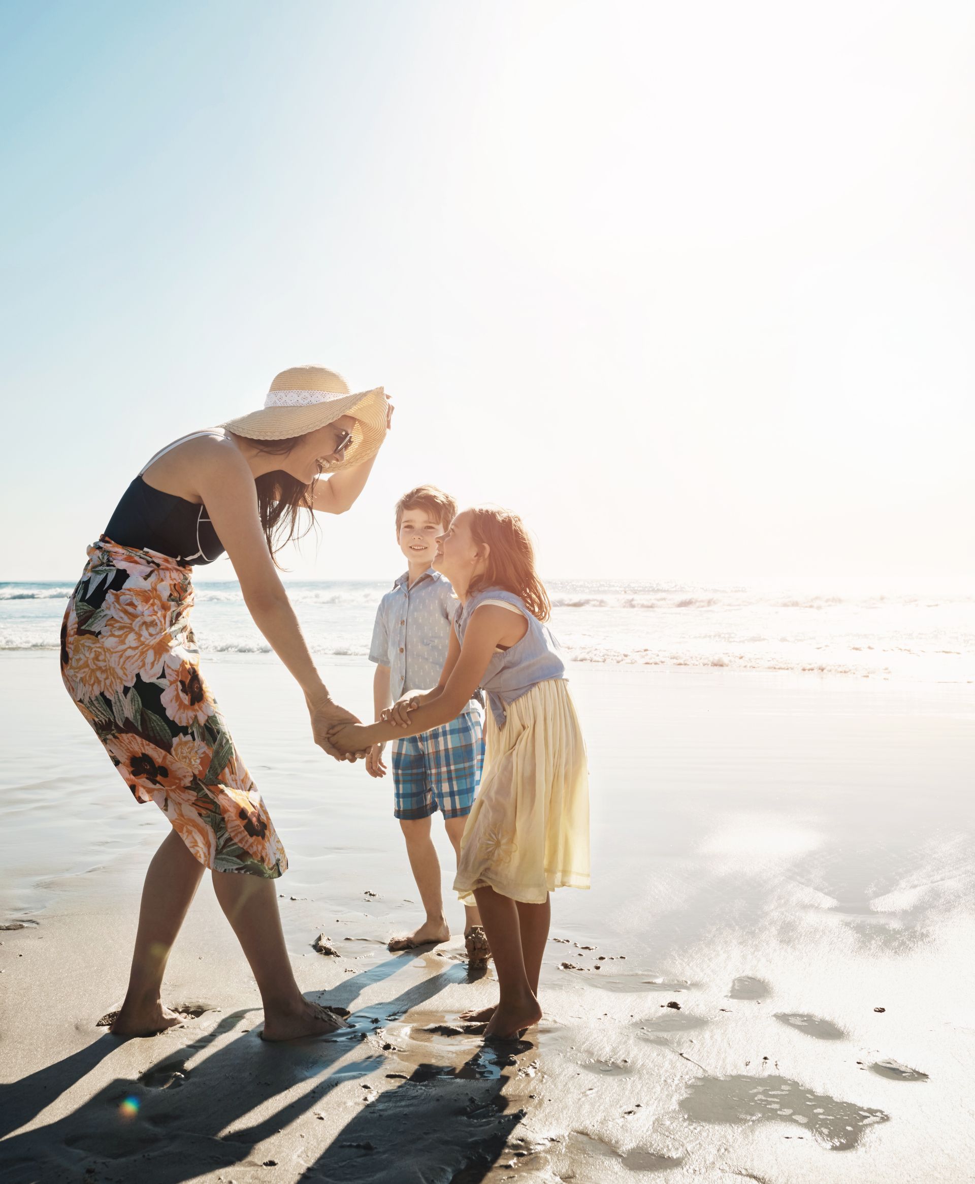 A woman is holding hands with two children on the beach.