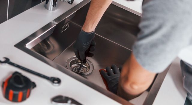 Un plombier nettoie un évier de cuisine avec une ventouse.