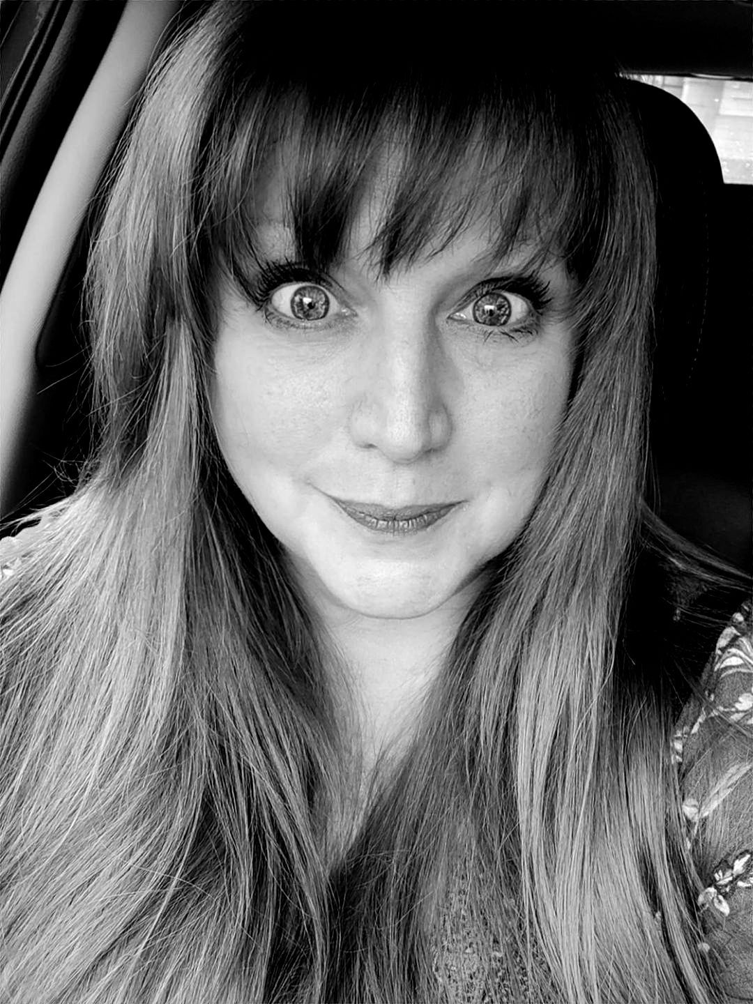 A woman with long hair and hoop earrings is smiling in a black and white photo.