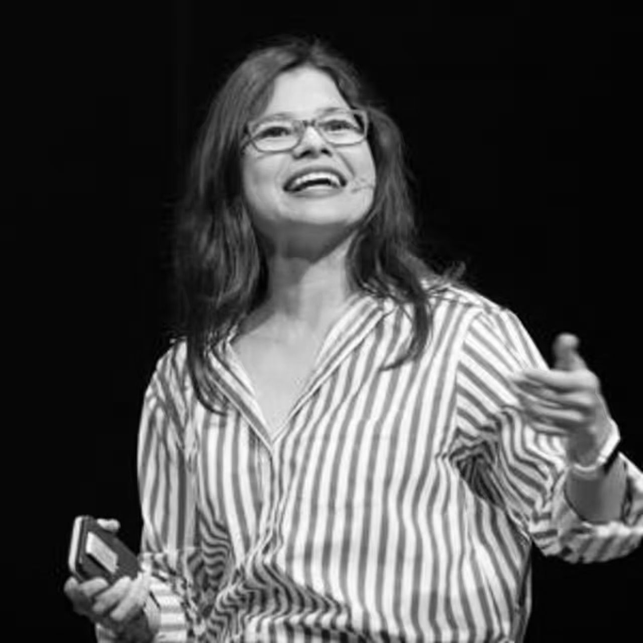 A woman wearing glasses and a striped shirt is holding a cell phone.