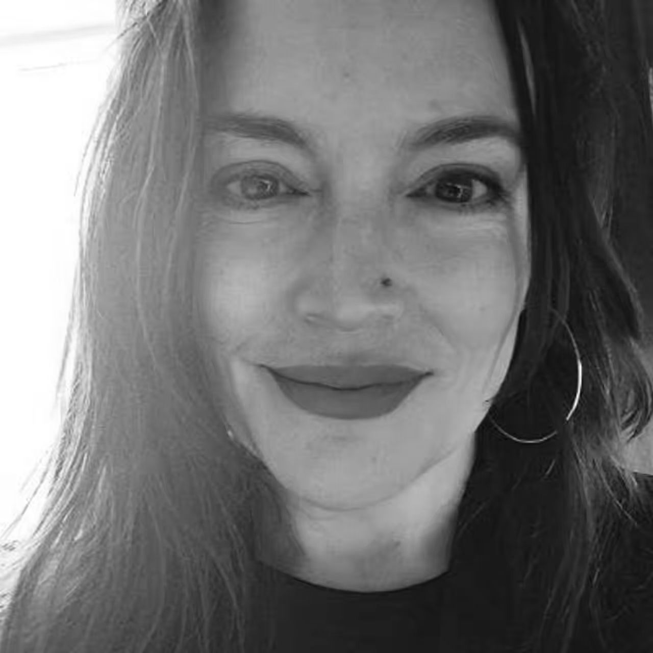 A woman with long hair and hoop earrings is smiling in a black and white photo.