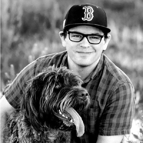 A man with a beard and glasses is smiling in a black and white photo.