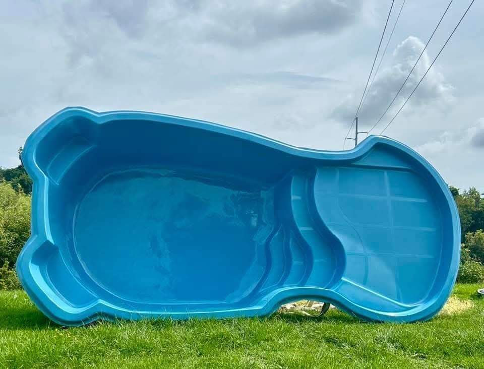 Blue fiberglass swimming pool on green grass with a cloudy sky backdrop.