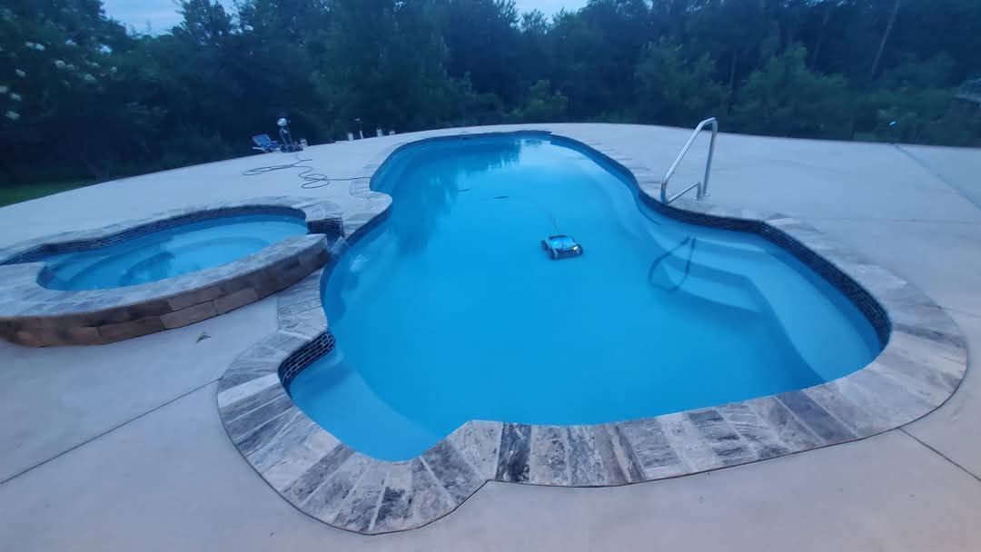 Pool with attached spa, both filled with blue water. Stone edging, gray concrete surround.