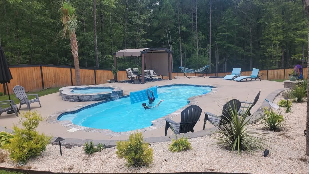 Backyard pool with lounge chairs, a spa, and a bamboo fence surrounded by trees.