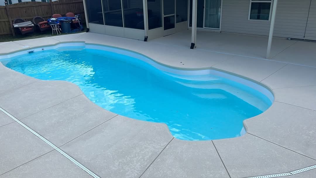 Swimming pool filled with clear blue water, surrounded by concrete patio.