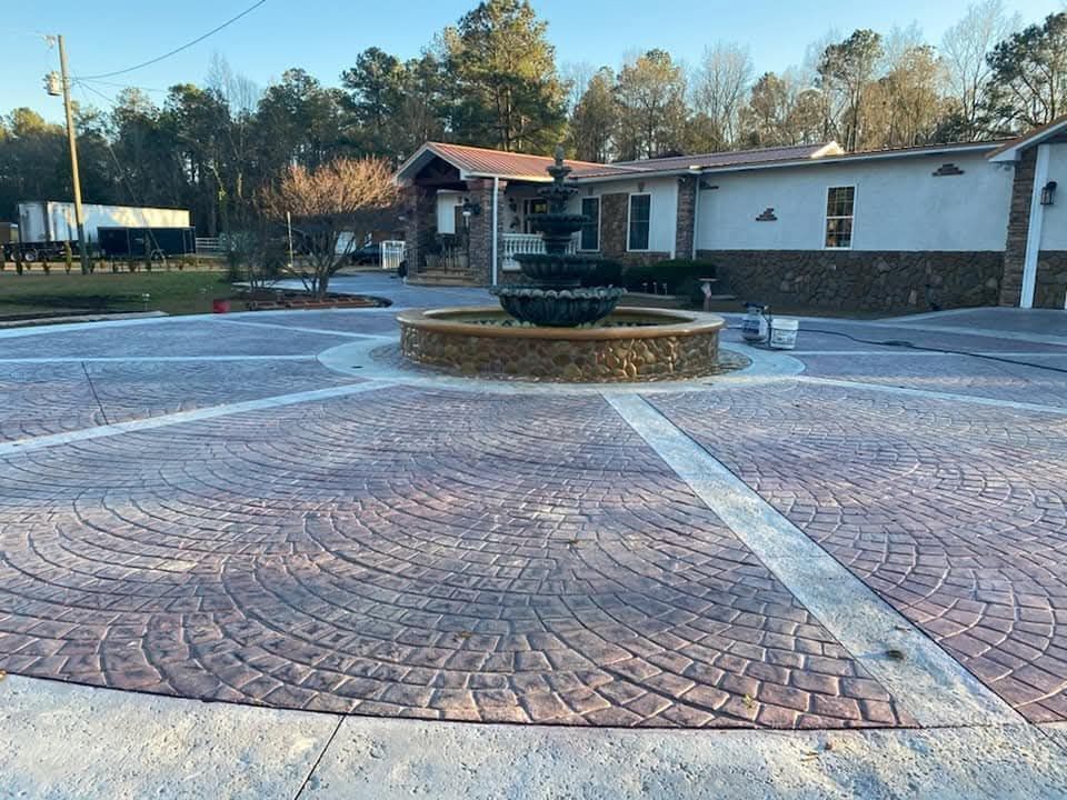 Stamped concrete driveway with fountain in front of a building; brick-like pattern, brown and gray tones.