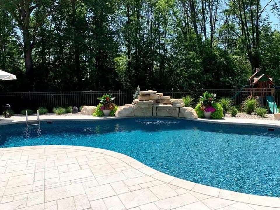 Pool with rock waterfall, surrounded by landscaping, fence, and trees.