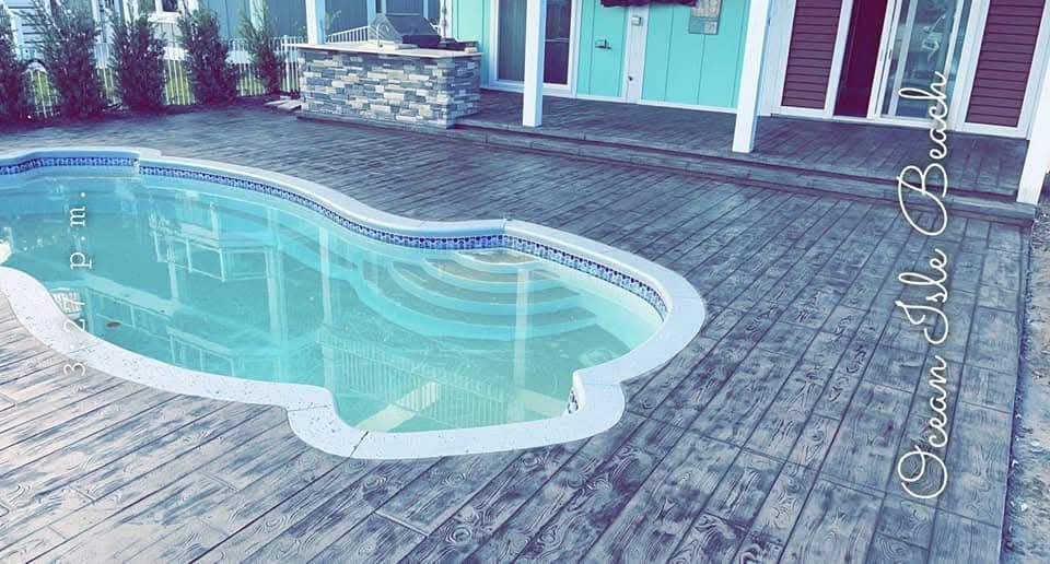 Swimming pool and wooden deck outside a teal-colored house.