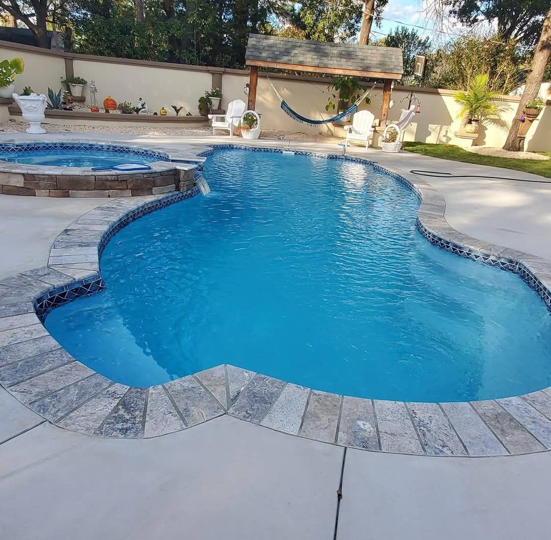 Pool with blue water and stone edging, next to a spa. A hammock and chairs are set up nearby.
