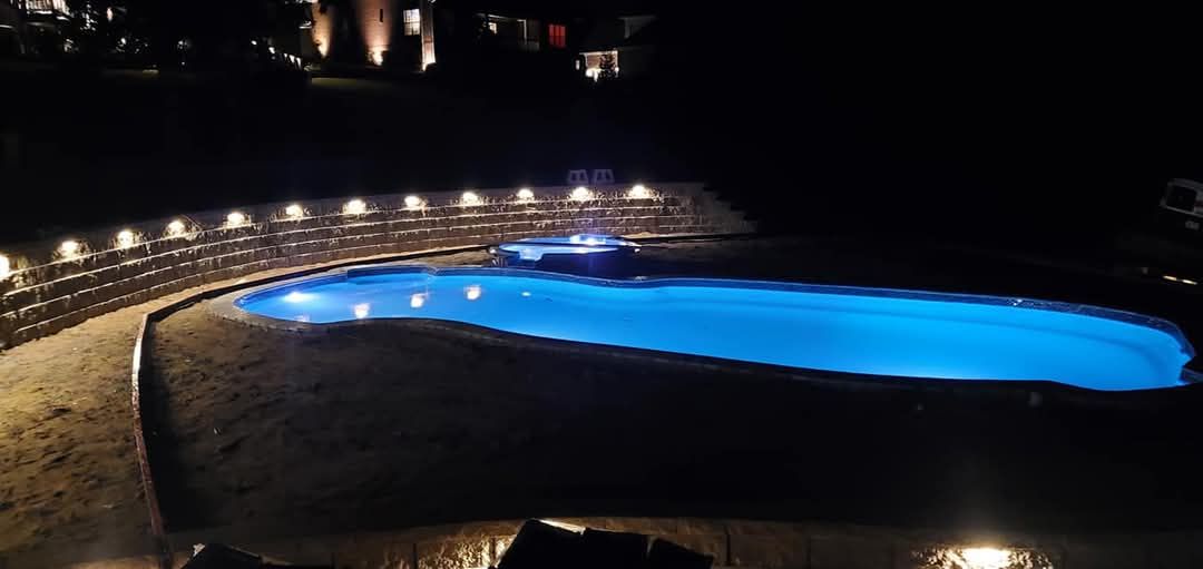 Nighttime view of a pool with blue water and lights around the edge.