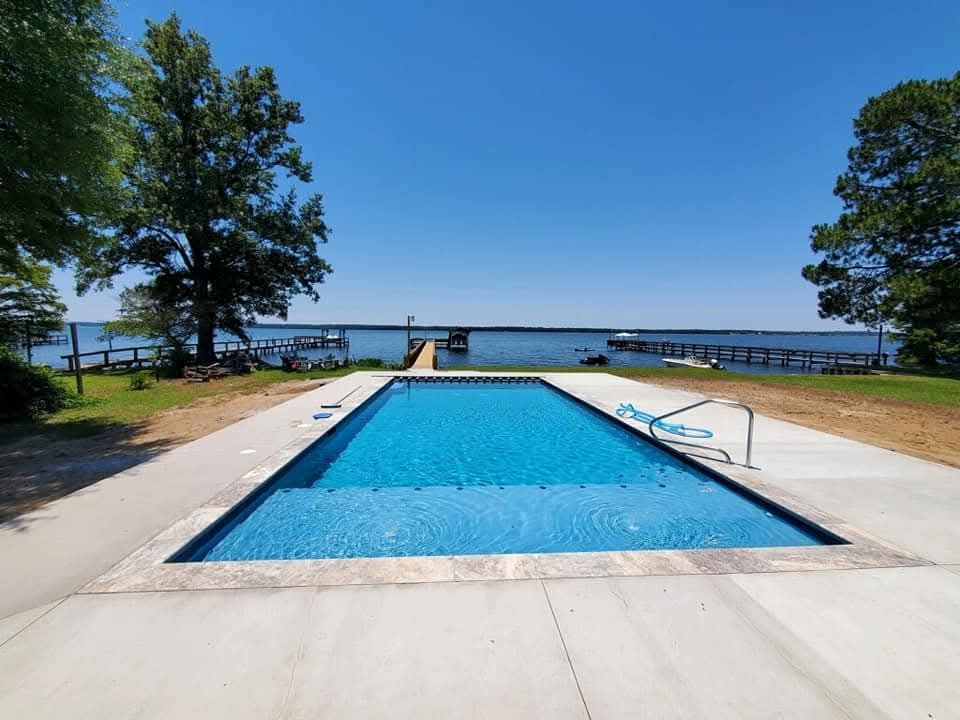 A rectangular blue pool next to a lake under a clear blue sky.