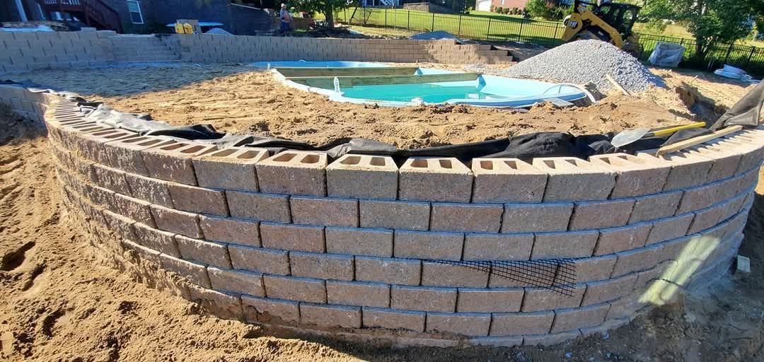 A partially built curved retaining wall surrounding a pool under construction.