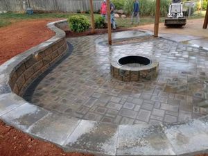 Newly constructed patio with fire pit and retaining wall, workers in background.