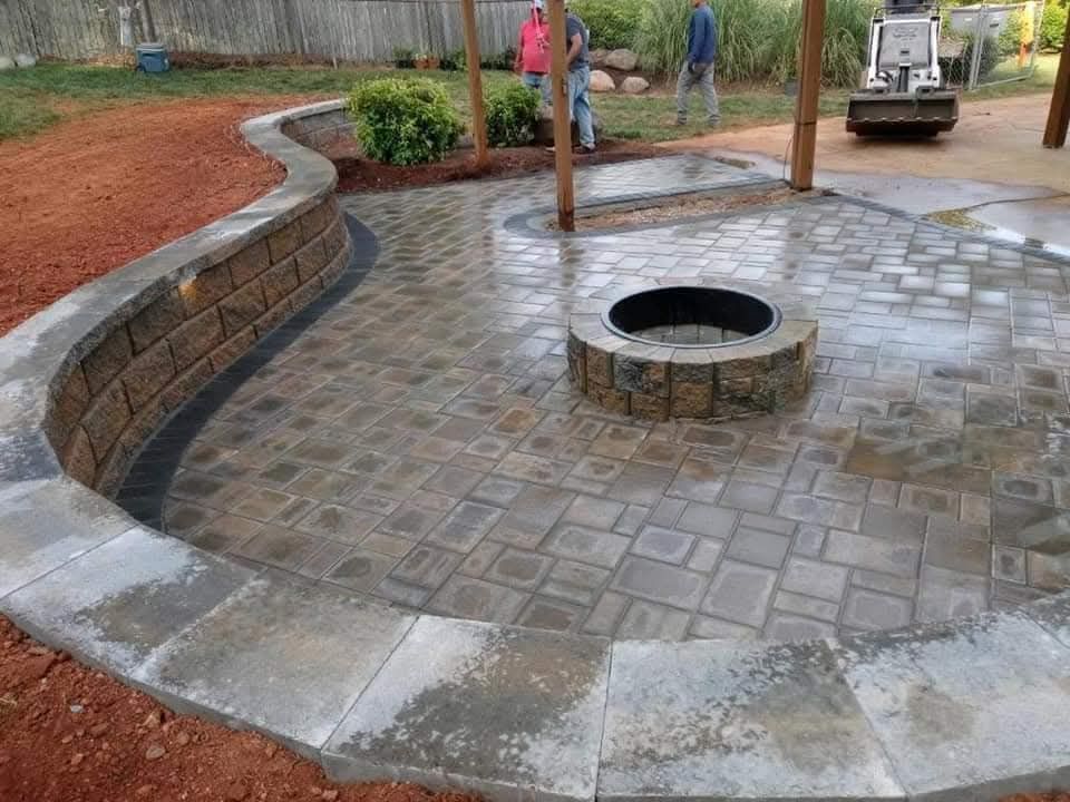 Finished patio with fire pit, retaining wall, and workers in background.
