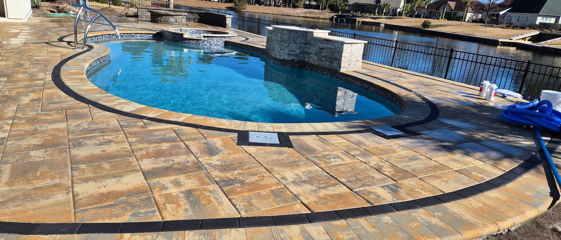 A swimming pool with blue water surrounded by stone pavers. A dark border frames the pool's edge.