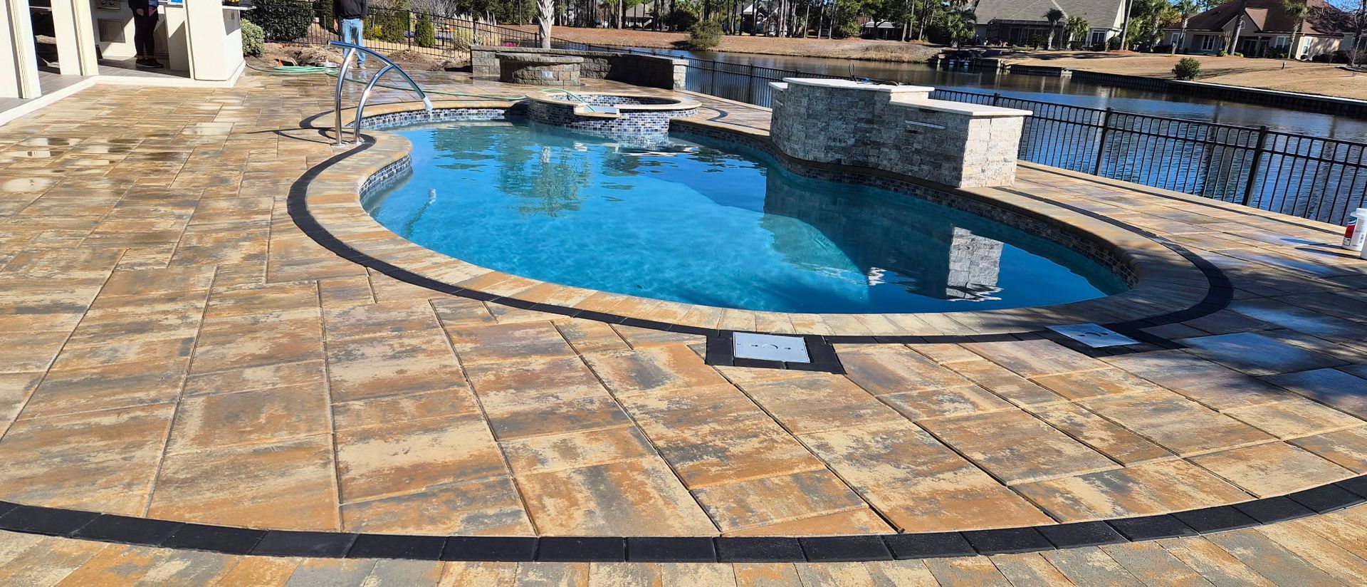 Stone patio surrounds a blue swimming pool with a stone water feature.