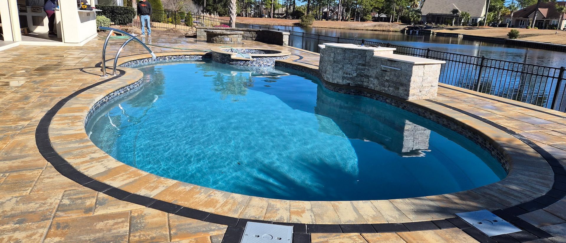 A kidney-shaped swimming pool with stone deck. The water is bright blue, reflecting the sky.