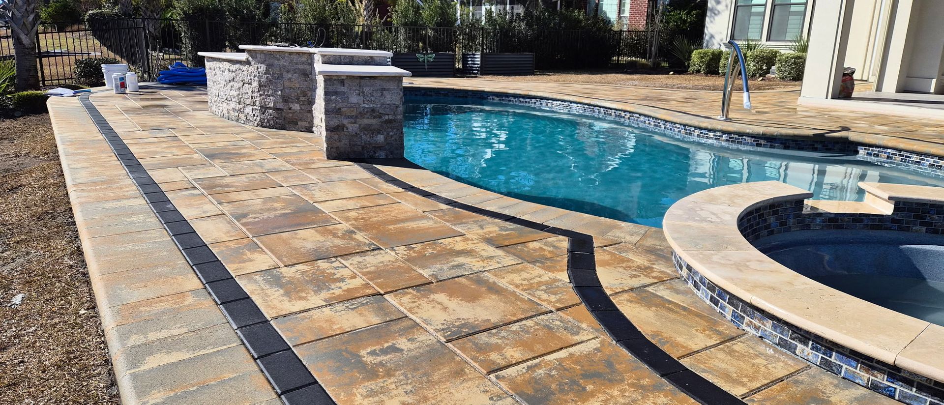 Backyard with a swimming pool, pavers, and stone structures.