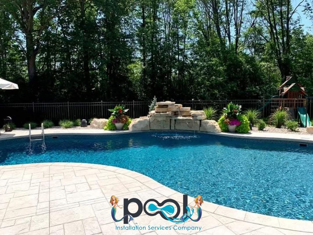 Swimming pool with rock waterfall feature, surrounding trees, and stone deck.