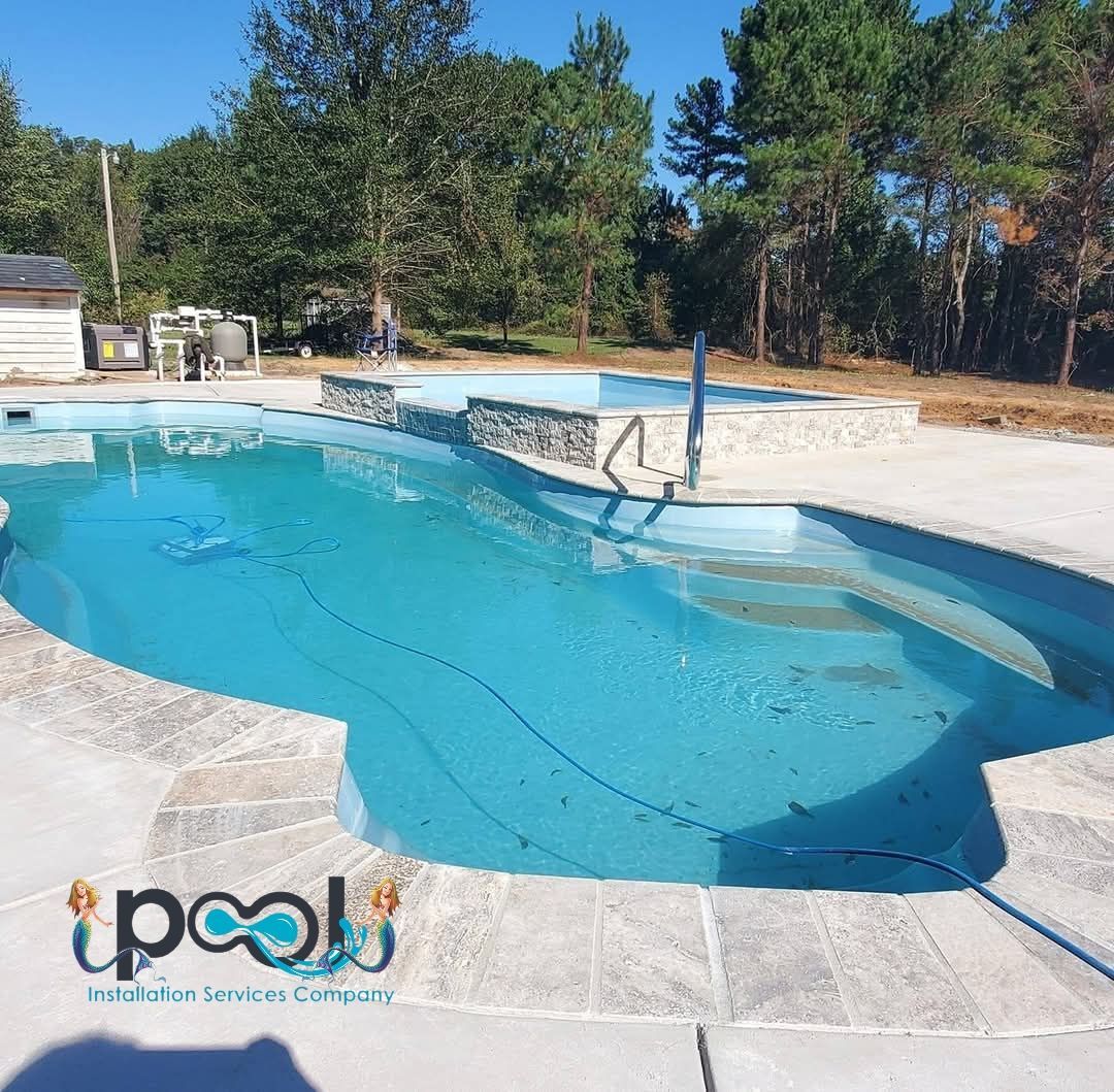 Pool with light blue water and stone coping on a sunny day. Equipment is visible in the background.