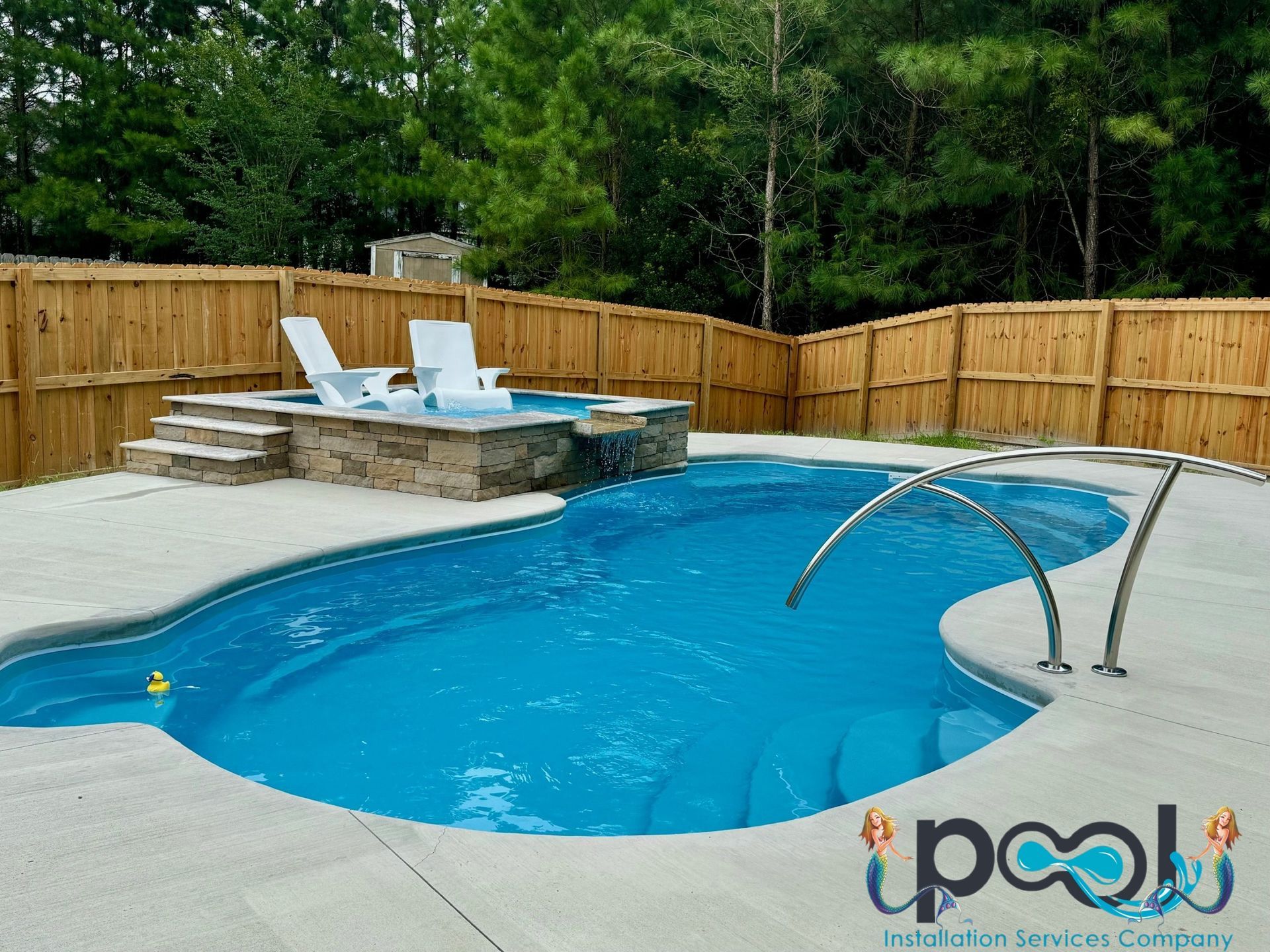 A blue swimming pool with a connected jacuzzi. Stone steps lead to the jacuzzi. Wooden fence surrounds the yard.
